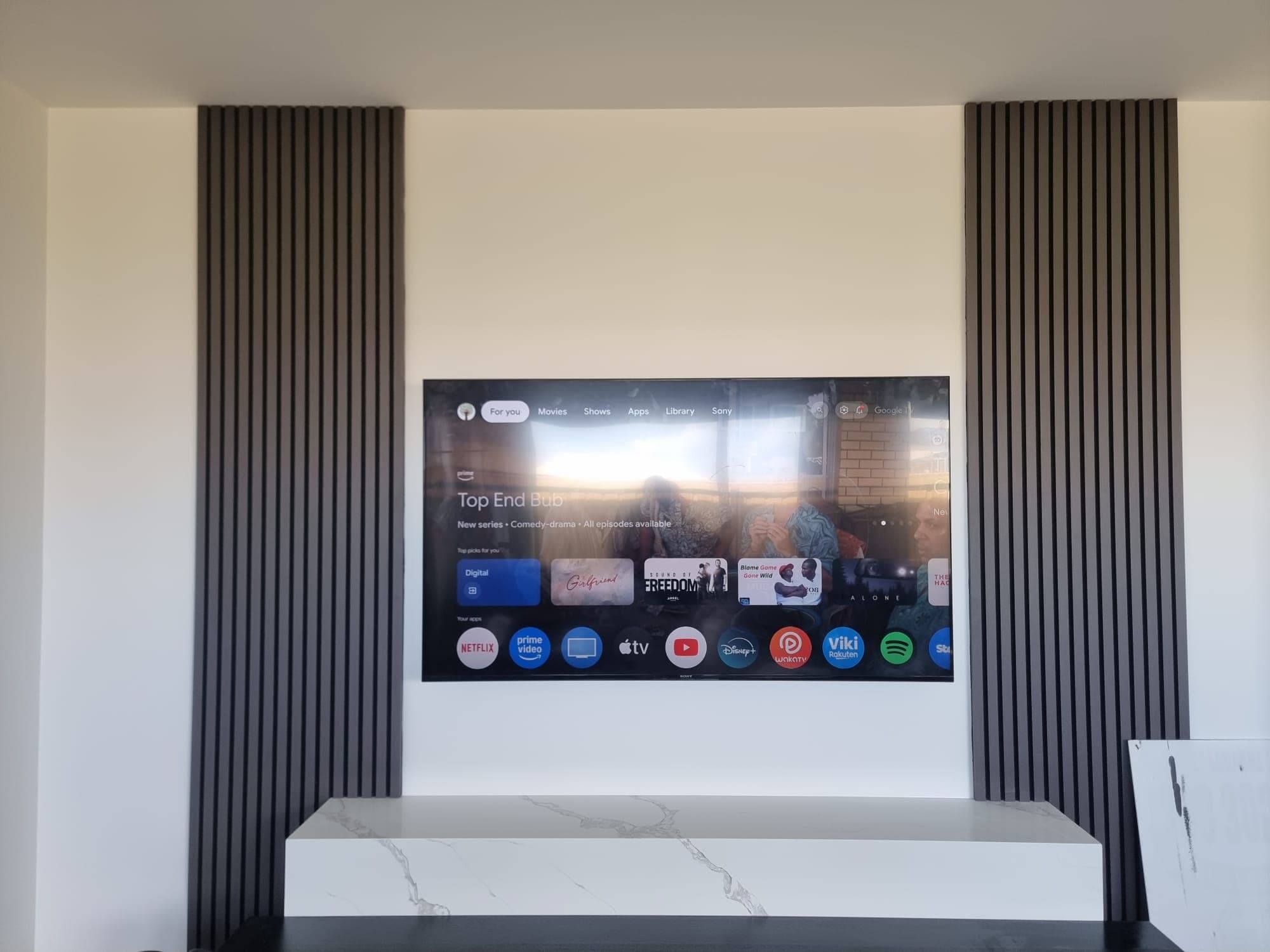 Google TV apps on a dark timber slat wall