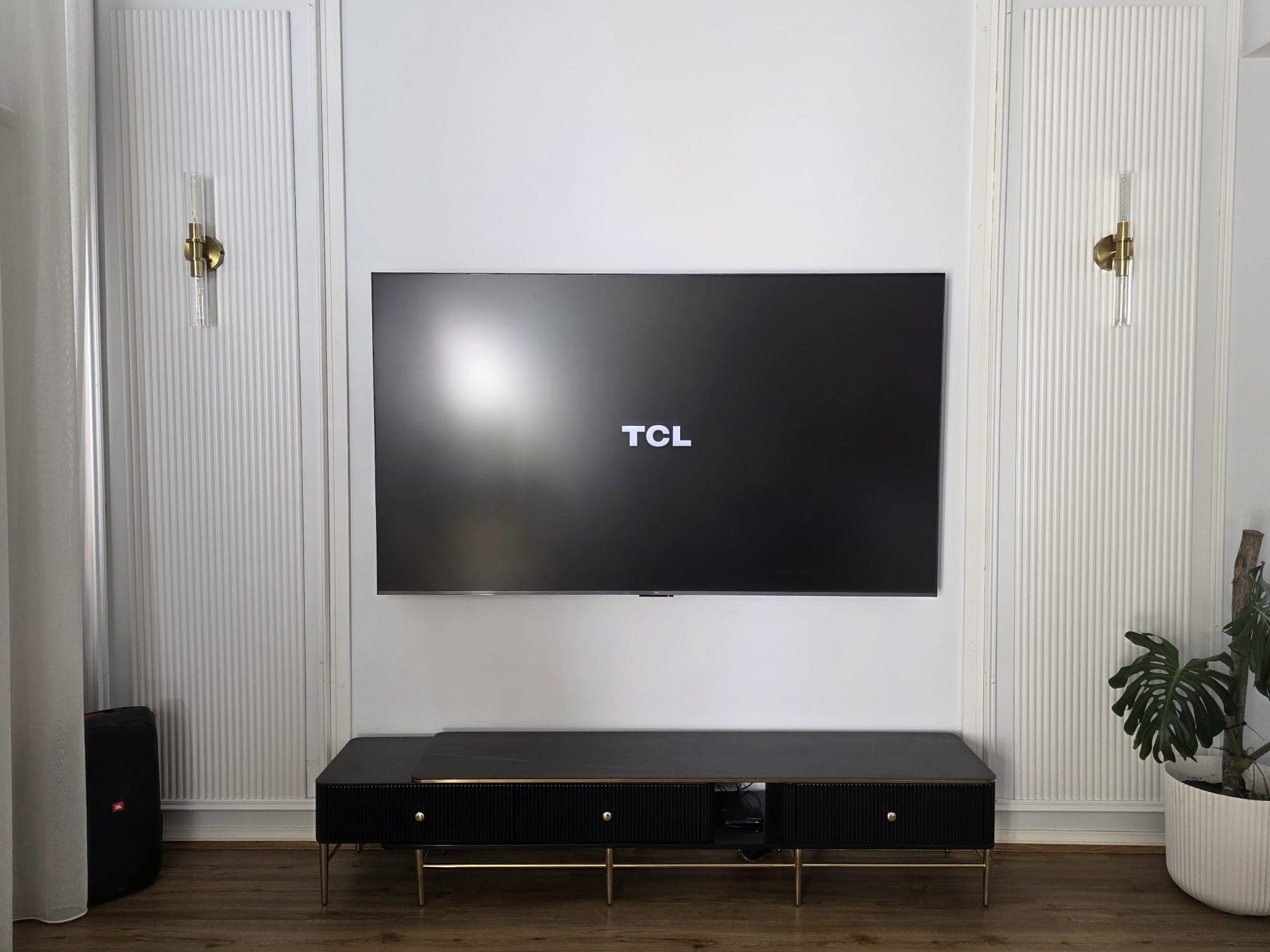 TCL TV on fluted wall panels with gold sconces